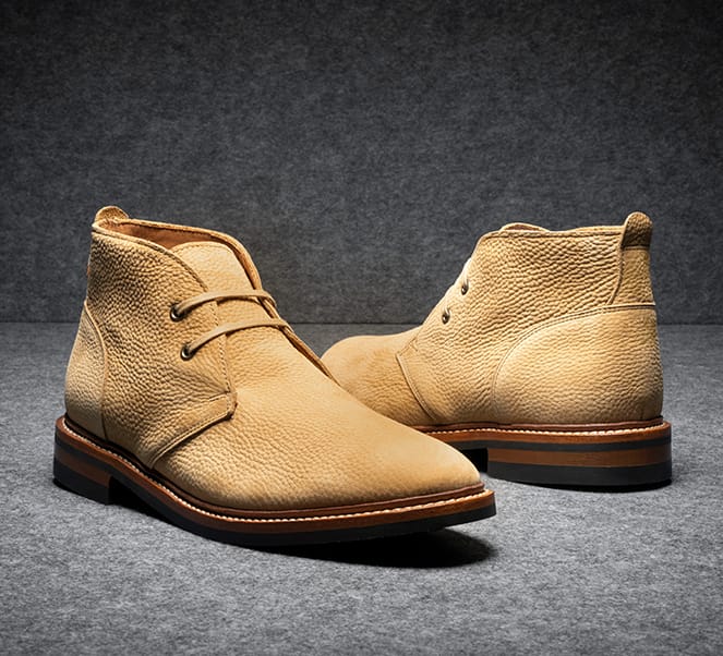 A pair of tan suede chukka boots displayed at an angle to show the front and back of the boot.  
