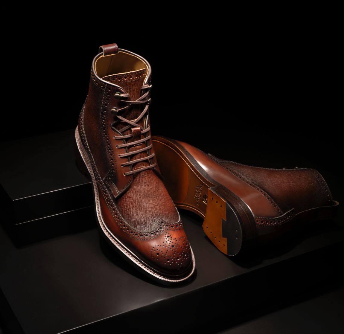 A pair of wingtip dress boots in brown leather, with one boot laying on its side.   