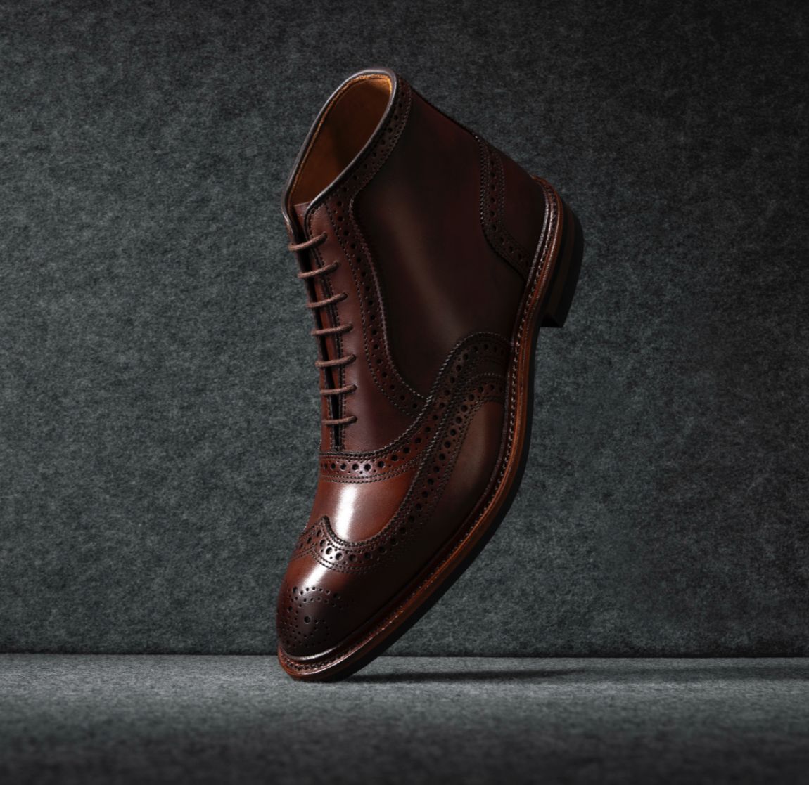 One brown leather wingtip dress boot displayed vertically with the toe facing downward.  