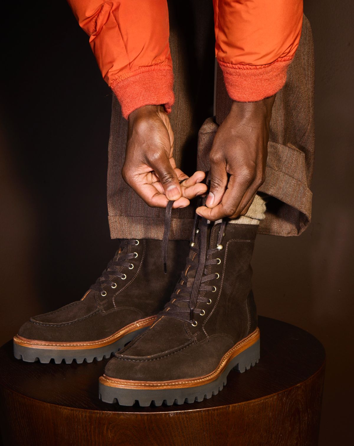A close-up view of a model tying the laces of a pair of brown suede lug sole boots.  