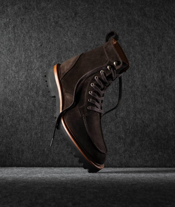 A men’s brown lug sole boot displayed vertically with the toe facing downward and laces untied.     