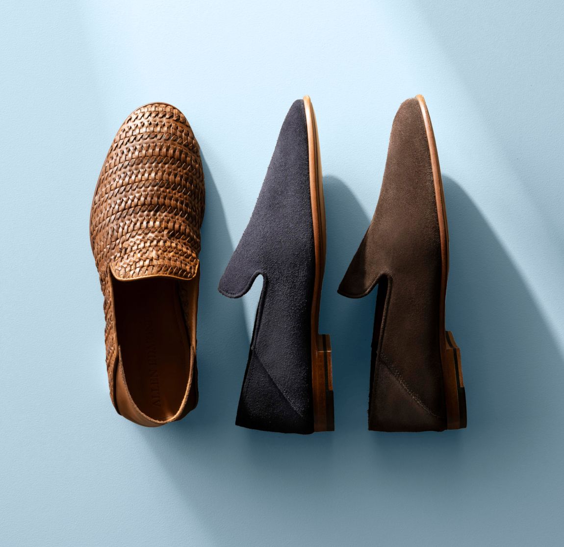 Chili woven leather, navy suede, and dark brown suede Allen Edmonds Portofino loafers against a light blue background 